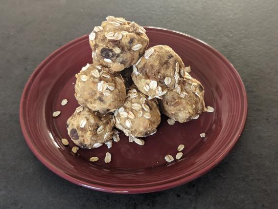 Pyramid of tan colored balls, dotted with chocolate chips, encrusted with rolled oats, on a red/brown plate.